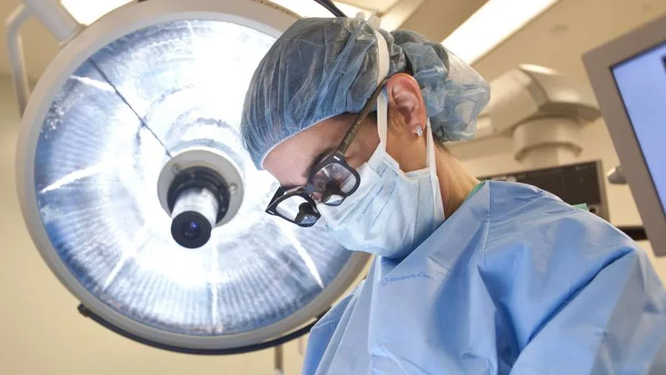 Photo of Doctor in surgery with surgical lamp behind them 