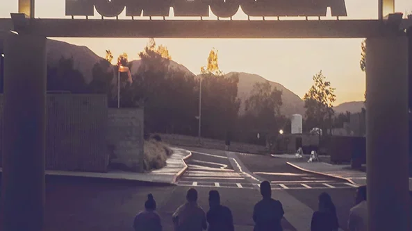 Five people sitting on the ground in front of an ambulance bay, with the word "AMBULANCE" mirrored above them. They are watching the sunset.