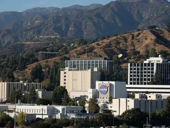 JPL Several buildings, including a prominent one with the NASA logo, located against a backdrop of mountainous terrain.