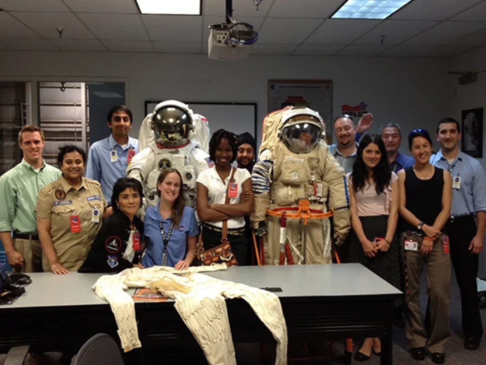Group of people posing in a classroom or lab setting. Two individuals are wearing astronaut suits.