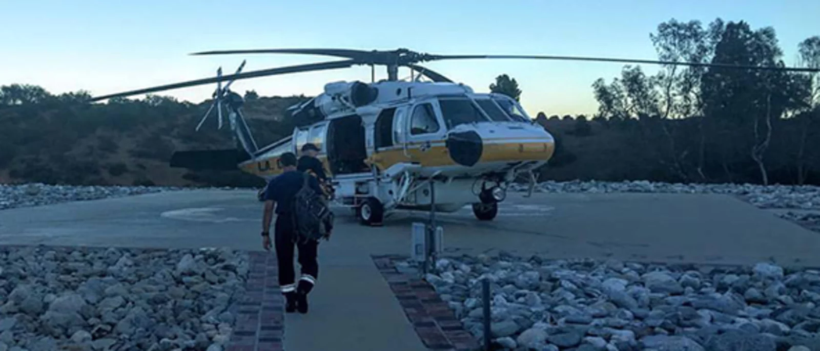 Helicopter on a helipad, with a person walking towards it. 