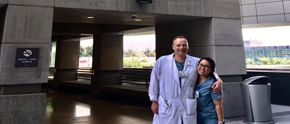 Two medical professionals standing in front of the entrance to the "David I. Saperstein Critical Care Tower" at Cedars-Sinai