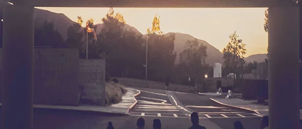 Five people sitting on the ground in front of an ambulance bay, with the word "AMBULANCE" mirrored above them. They are watching the sunset.